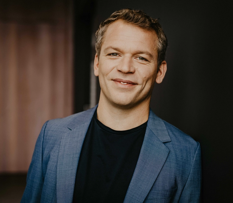A man dressed in a blue jacket and black shirt poses